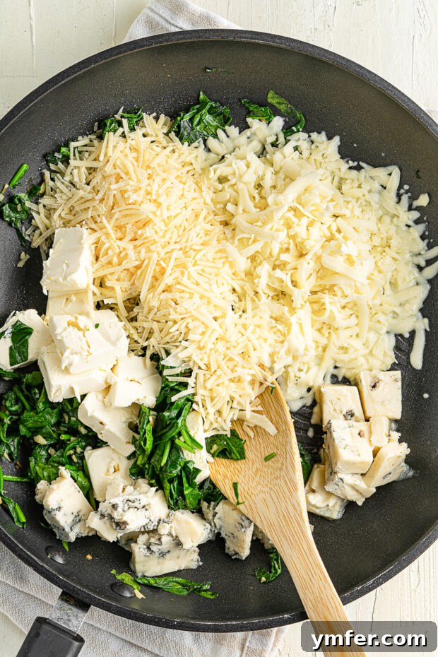 Creamy Cheesy Butternut Squash Bake 4 Skillet filled with melted cheeses and vibrant spinach, ready to be mixed with squash.