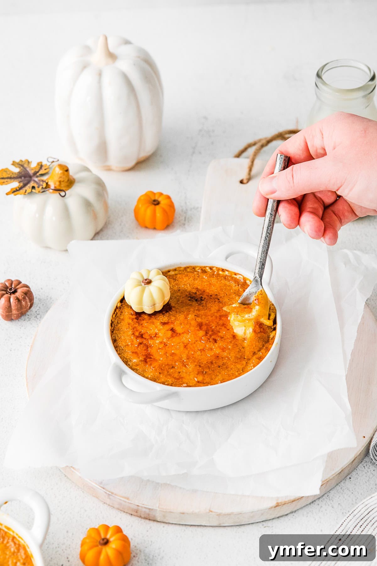 Spiced Pumpkin Creme Brulee 10 A hand holding a spoon about to take a bite of Pumpkin Creme Brulee, showing the creamy custard texture.