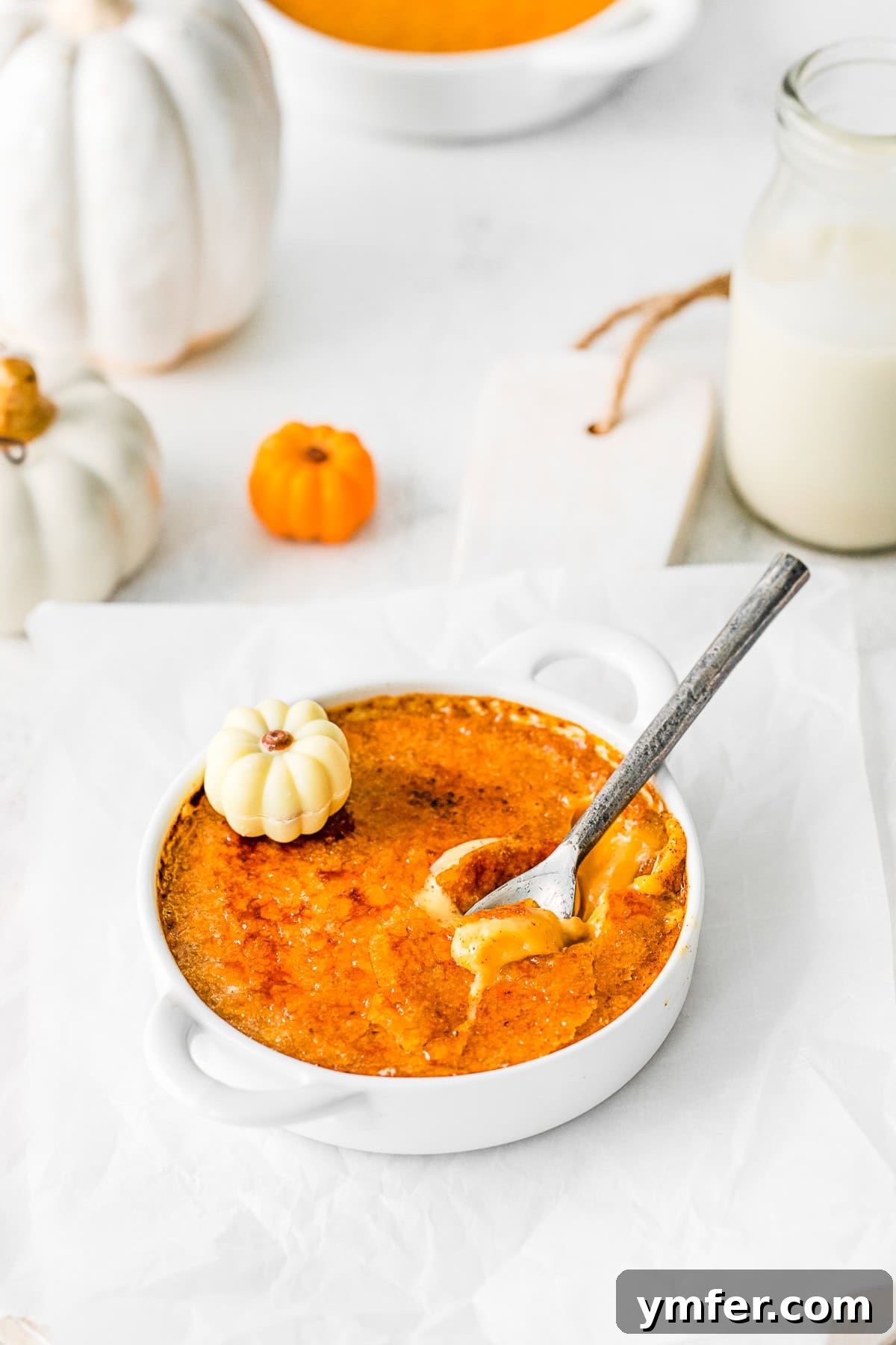 Spiced Pumpkin Creme Brulee 4 A spoon cracking through the caramelized sugar topping of a Pumpkin Creme Brulee, revealing the creamy custard beneath.
