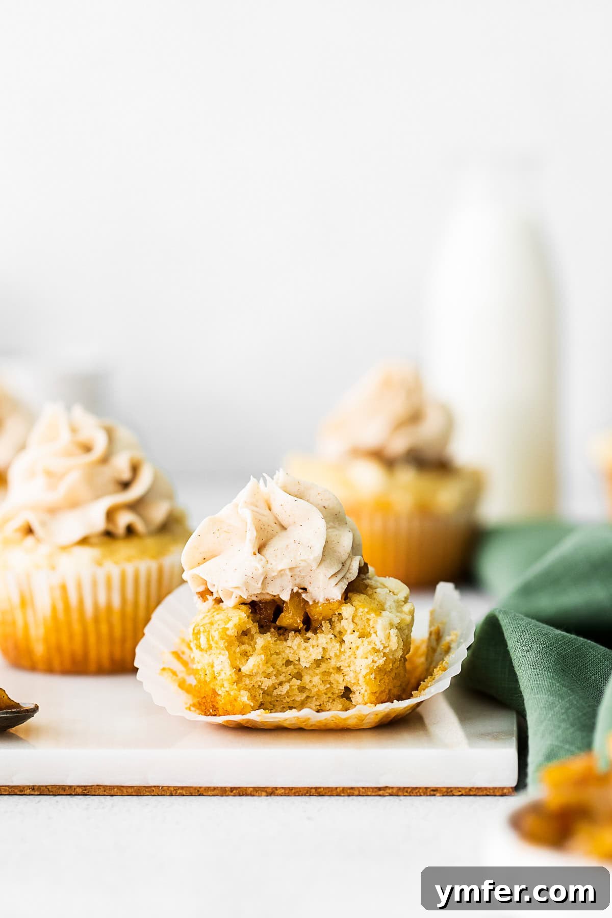 Cinnamon Apple Pie Cupcakes 7 A beautiful Apple Pie Cupcake with a bite taken out, revealing the delicious, spiced apple filling inside, surrounded by cake and topped with frosting.