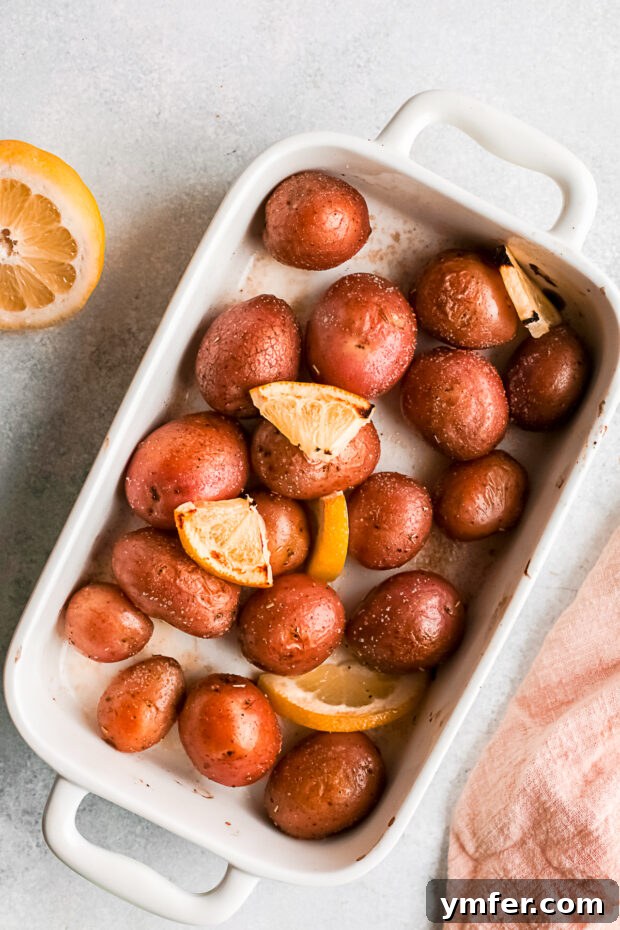 Golden Gooey Smashed Potatoes 5 Whole roasted baby red potatoes with lemon slices scattered around them in a white baking dish.