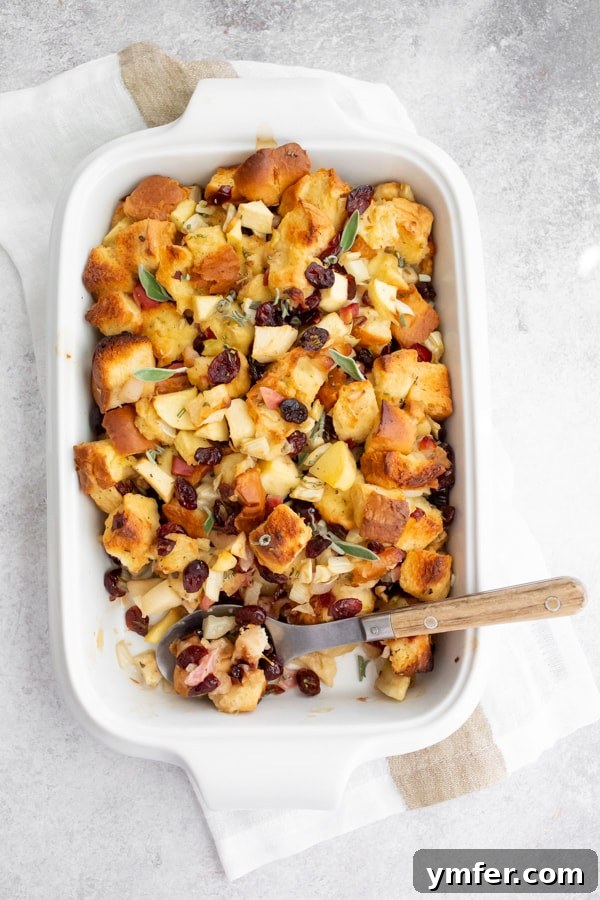 A Feast of Thanksgiving Sides 29 Gourmet Pancetta Apple Fennel Brioche Stuffing baked in a small white casserole dish, featuring a golden-brown crust.