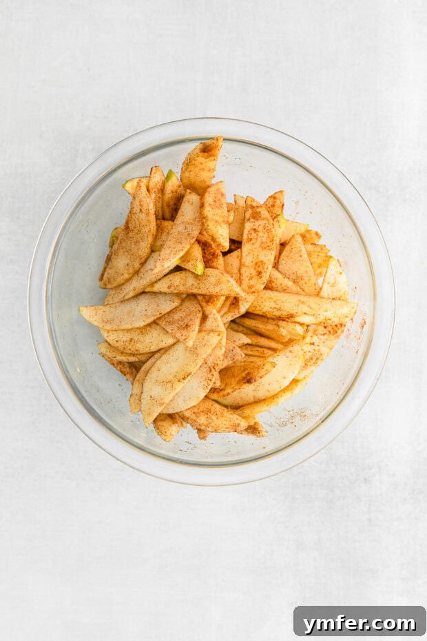 Sliced apples tossed with brown sugar, cinnamon, lemon juice, and cornstarch in a mixing bowl.