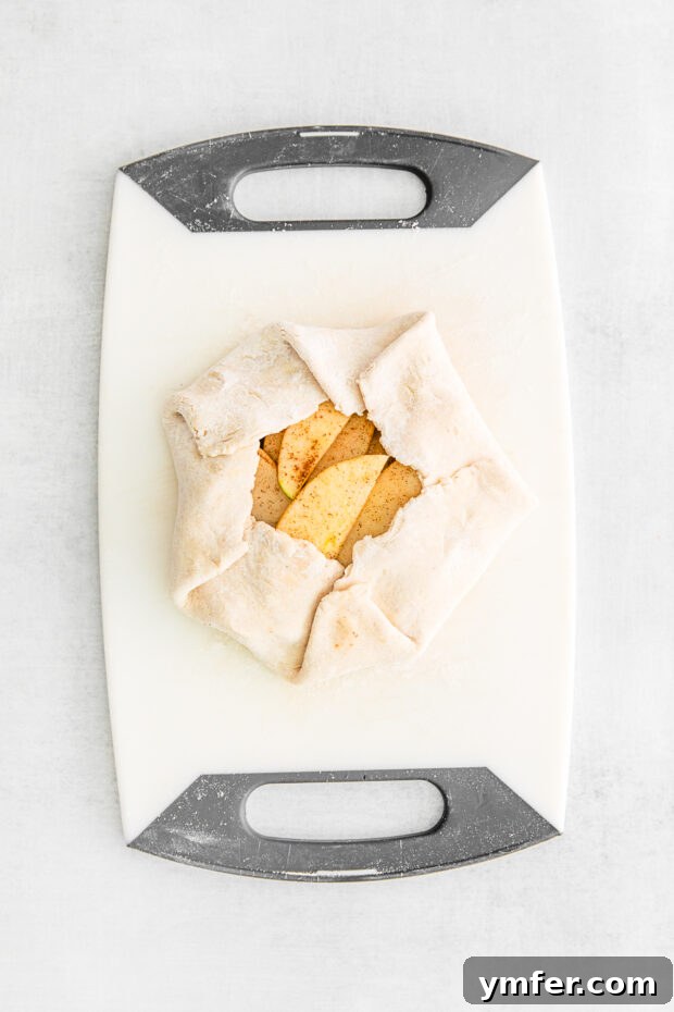 An uncooked mini apple galette, with a rustic folded crust, placed on a cutting board.