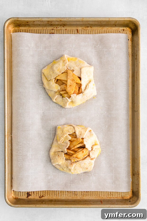 Uncooked mini apple galettes neatly arranged on a parchment-lined sheet pan, ready for baking.