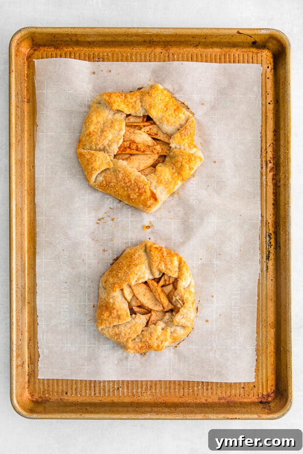 Freshly baked mini apple galettes with golden-brown crusts and bubbling apple filling on a sheet pan.