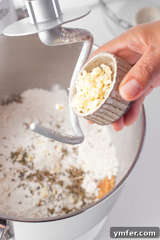 Warm Garlic Herb Rolls 5 Finely minced fresh garlic being added to the soft, developing bread dough in a stand mixer, ready to be incorporated for flavor.