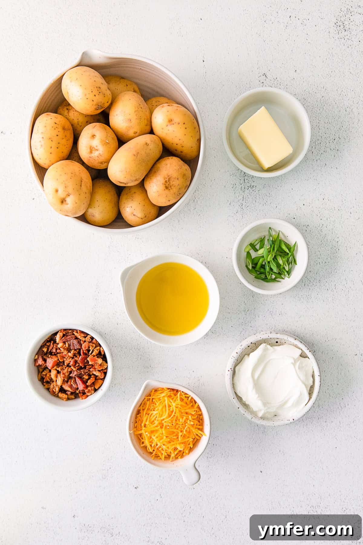 Tiny Tater Toppers 3 Various fresh ingredients laid out on a wooden table, including small yellow potatoes, a bowl of sour cream, cheddar cheese, butter, and fresh chives, ready for preparing Mini Loaded Baked Potatoes.