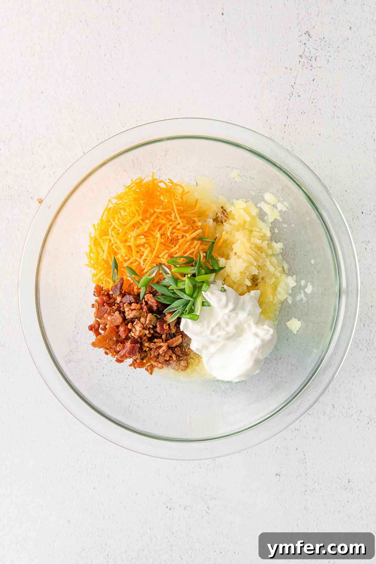 Tiny Tater Toppers 7 A bowl filled with a creamy mixture of mashed potatoes, sour cream, melted cheese, and bacon, ready to be stuffed into potato skins.