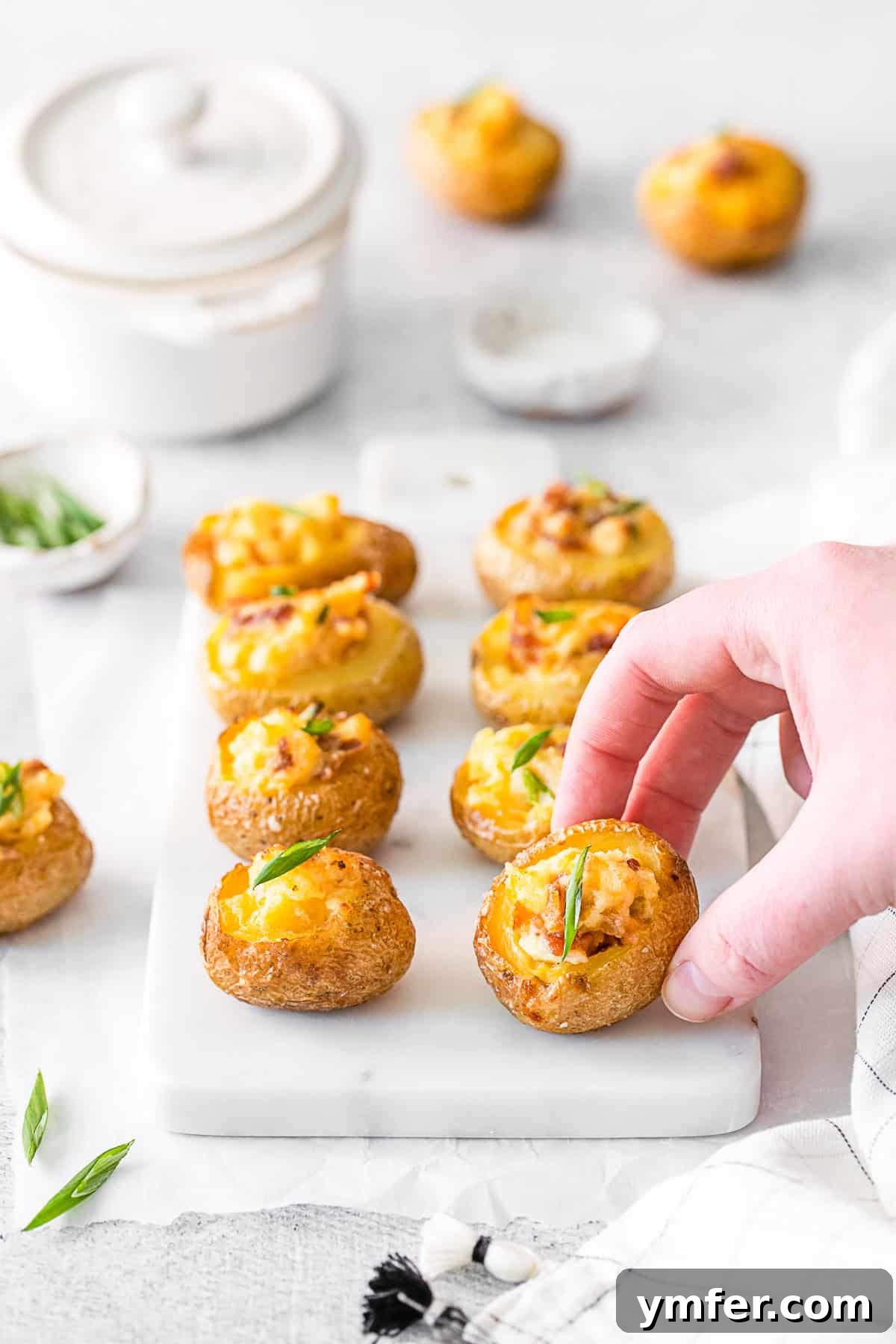 Tiny Tater Toppers 8 A hand reaching for a perfectly golden and stuffed Mini Loaded Baked Potato, showing its tempting texture.