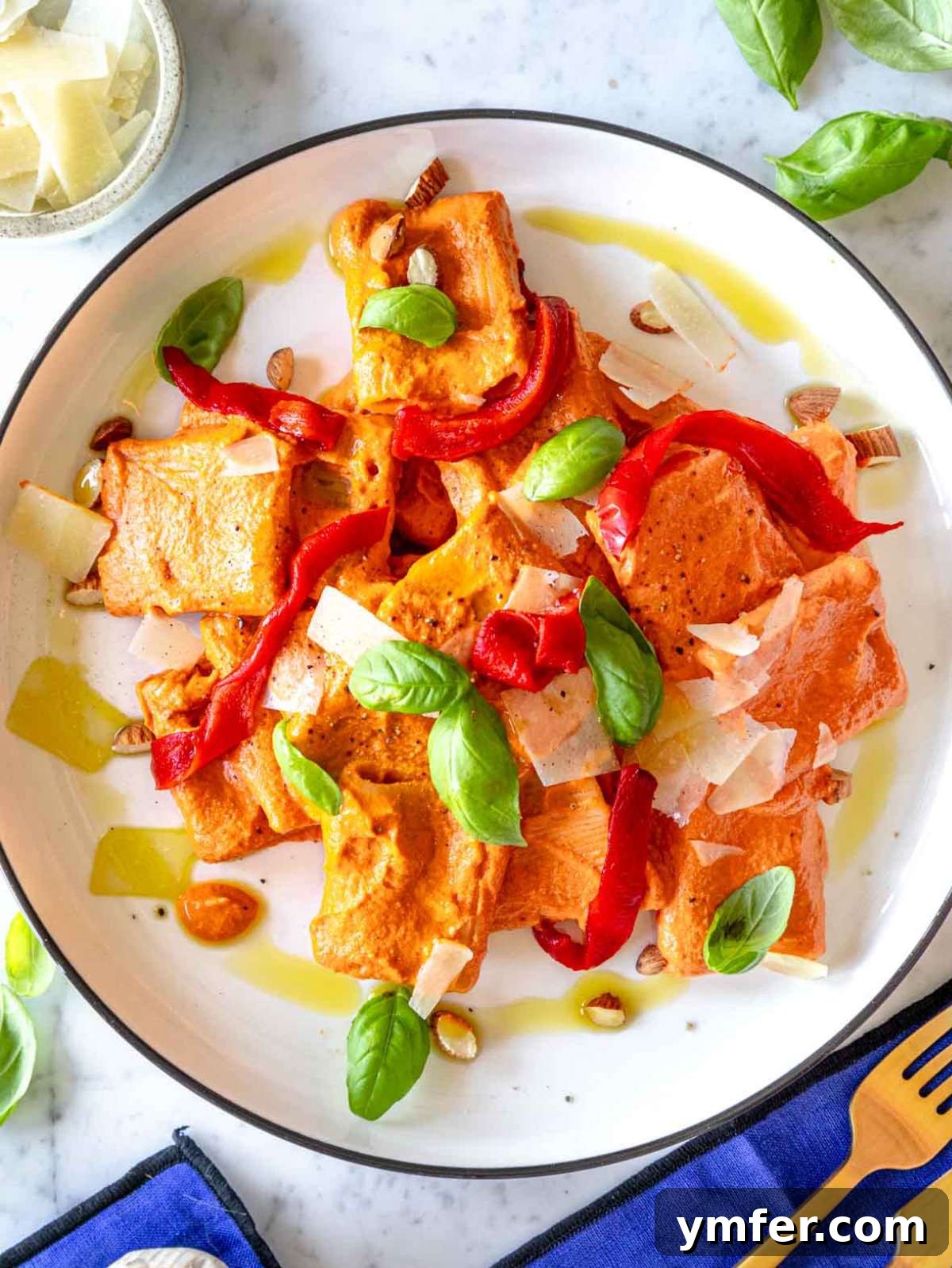 Vibrant Red Pepper Pasta 4 Top-down view of roasted red pepper pasta garnished with fresh basil leaves and a sprinkle of cheese, showcasing its rich, creamy texture.
