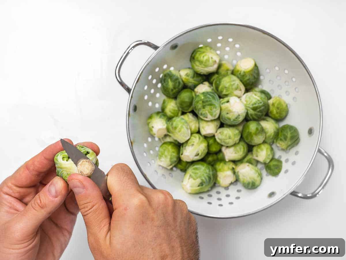 Crispy Roasted Brussels Sprouts 7 Close-up of a hand trimming the woody stem of a Brussels sprout with a paring knife.