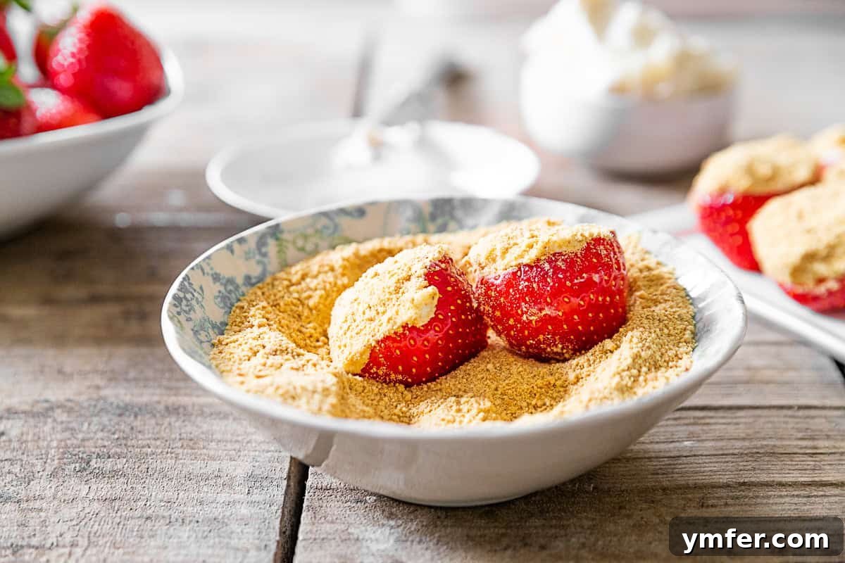 Strawberry Cheesecake Bliss Bites 5 Cheesecake Stuffed Strawberries in a bowl of graham cracker crumbs.