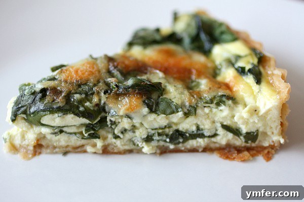Swiss Chard, Leek and Gruyere Quiche by Nutmeg Nanny A slice of Swiss Chard Leek Quiche on a white plate, revealing its creamy filling and golden crust.