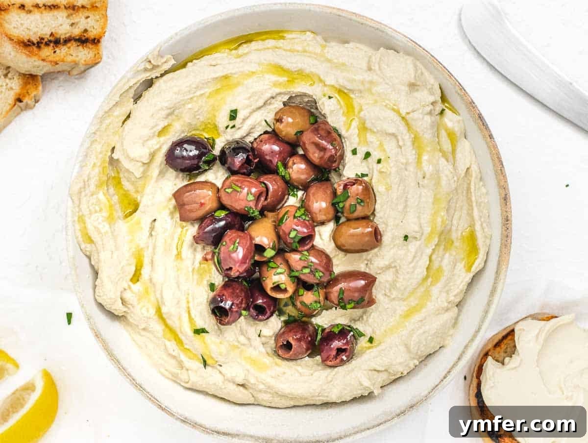 Bowl of speckled olive cream cheese, garnished with whole olives and herbs