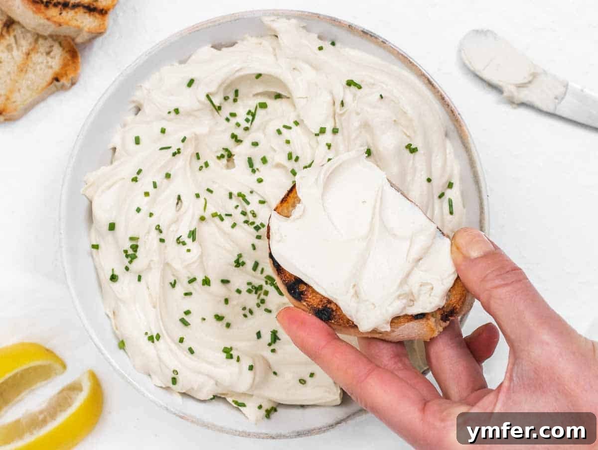 A hand holding a piece of toasted bread generously spread with white tofu cream cheese