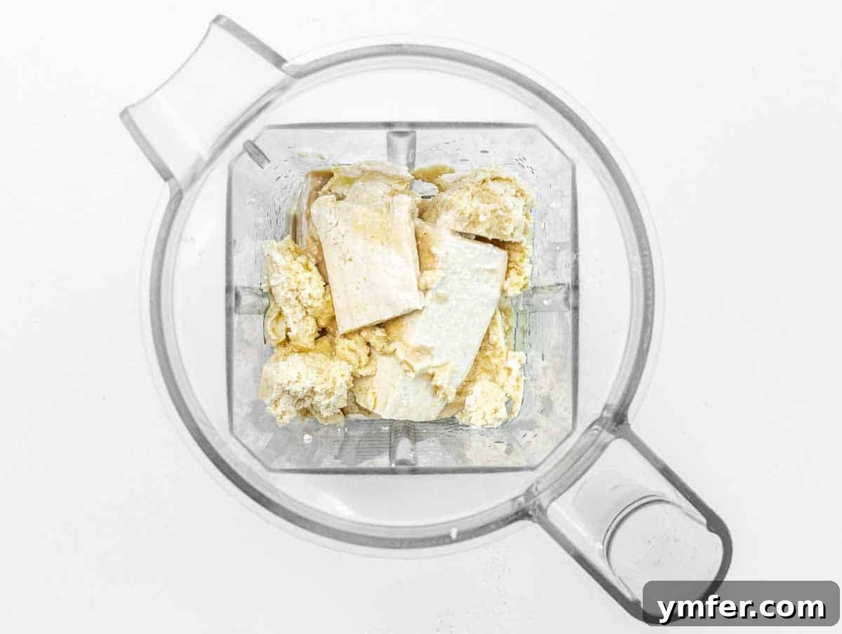 Close-up of tofu cubes, tahini, lemon juice, olive oil, and salt in a blender cup