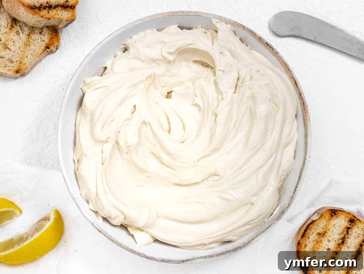 Bowl of white tofu cream cheese, with a lemon wedge and fresh herbs on the side