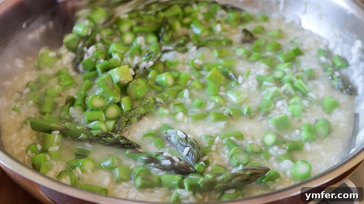 Effortless Plant-Based Risotto 13 A close-up of risotto cooking in a pot, being stirred frequently.