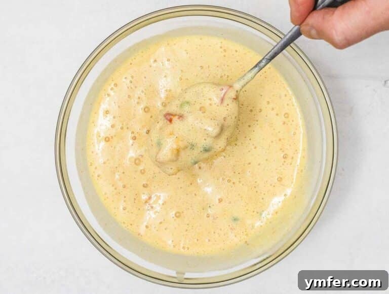 Wholesome Chickpea Egg Muffins 19 Chickpea Muffin batter with veggies and hand holding a spoon