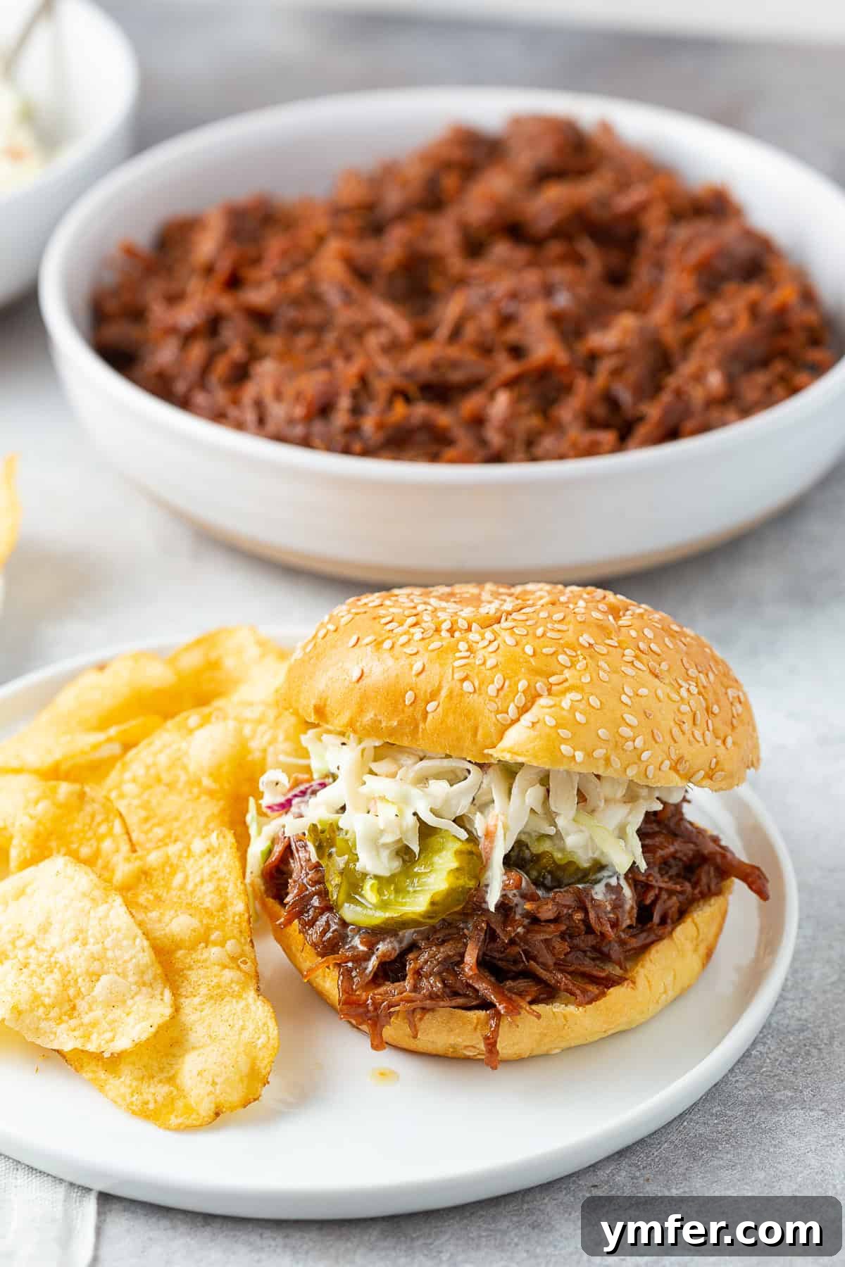 Smoky Pulled Beef Sandwiches 5 BBQ shredded beef on a bun with coleslaw and pickles, presented as a classic sandwich.