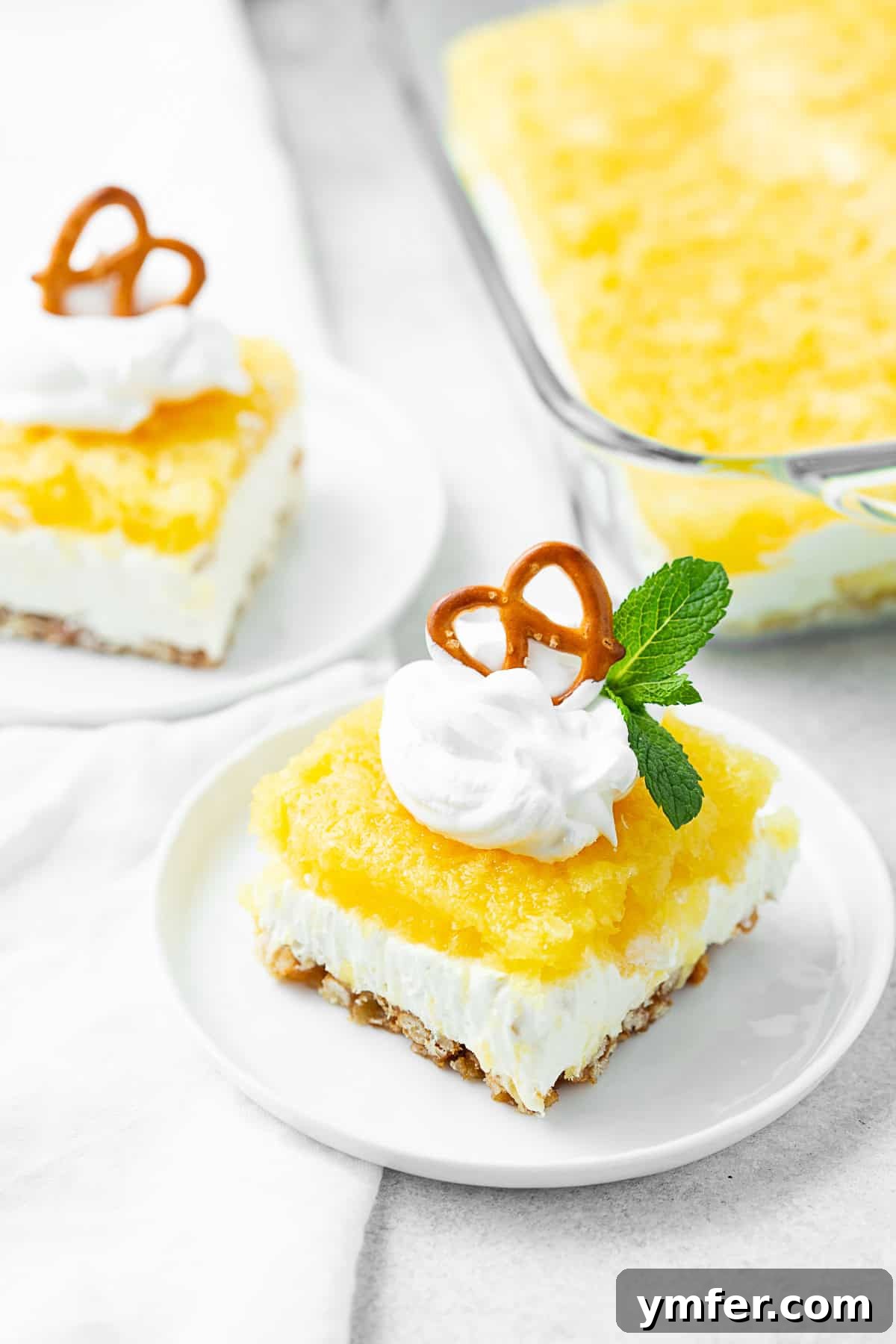 Tropical Pretzel Delight 2 A slice of vibrant Pineapple Pretzel Salad on a white plate, showcasing its distinct layers of crunchy pretzel crust, creamy filling, and glistening pineapple jello topping.