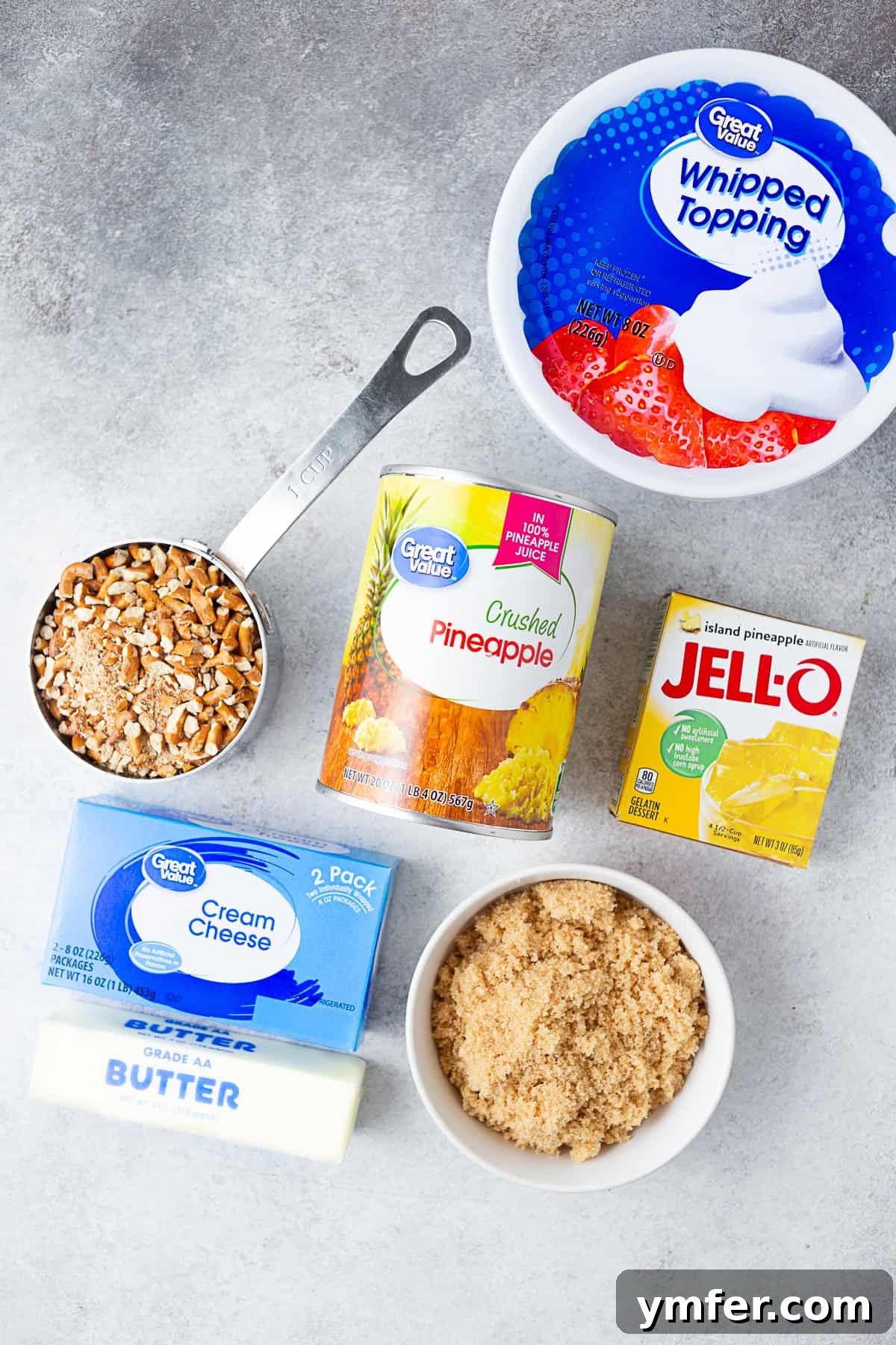 Tropical Pretzel Delight 3 Ingredients for Pineapple Pretzel Salad laid out on a table: cool whip, Jell-O powder, canned pineapple, sugar, cream cheese, and a bag of pretzels, ready for preparation.