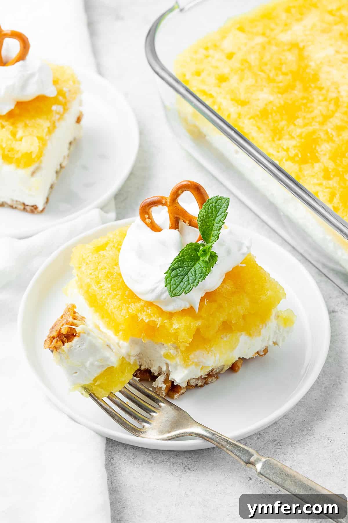 Tropical Pretzel Delight 5 A perfectly sliced piece of Pineapple Pretzel Salad resting on a white plate with a fork, ready to be enjoyed.