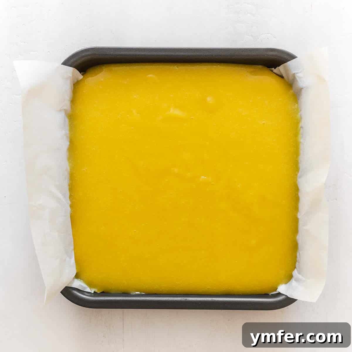 Zesty Plant-Based Lemon Squares 17 Smooth vegan lemon curd being poured and spread over the baked pie crust in a baking pan.