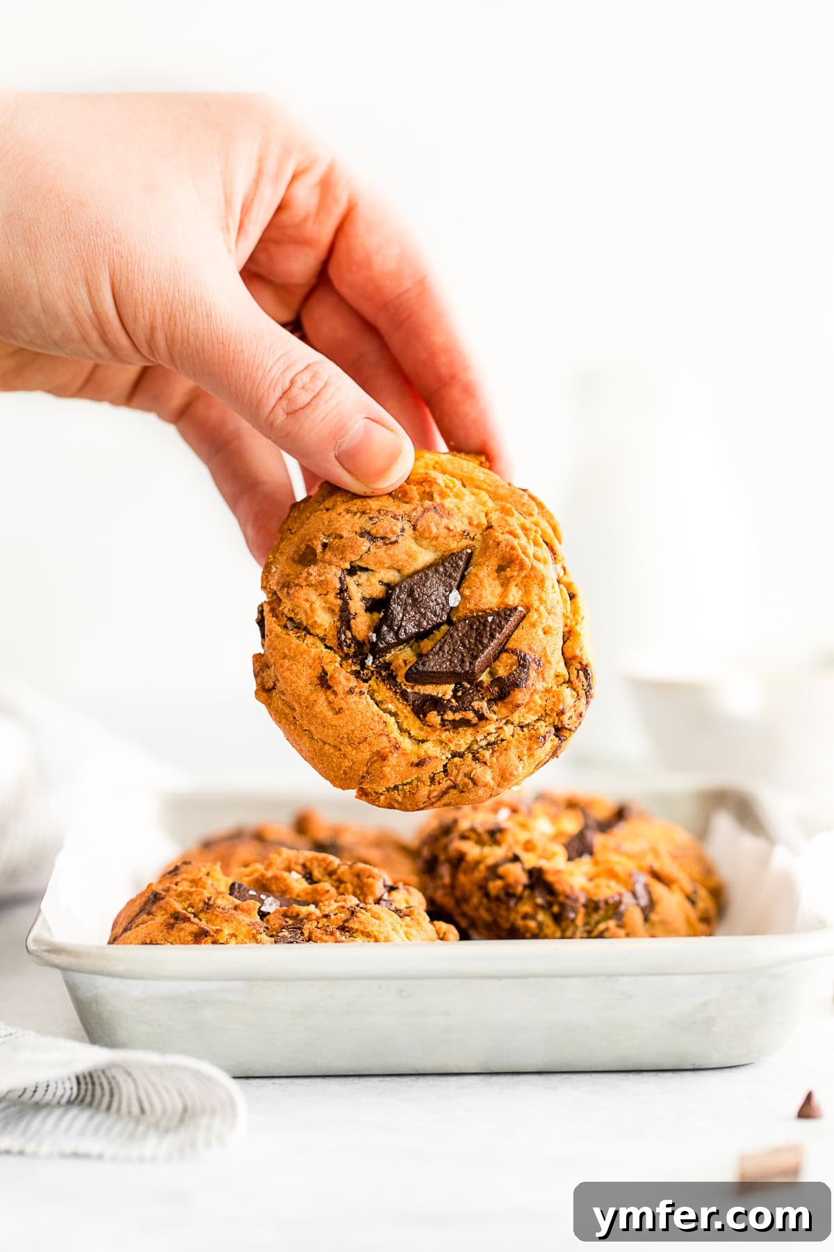 A hand holding a freshly baked, warm air fryer chocolate chip cookie, showcasing its soft texture and melted chocolate.