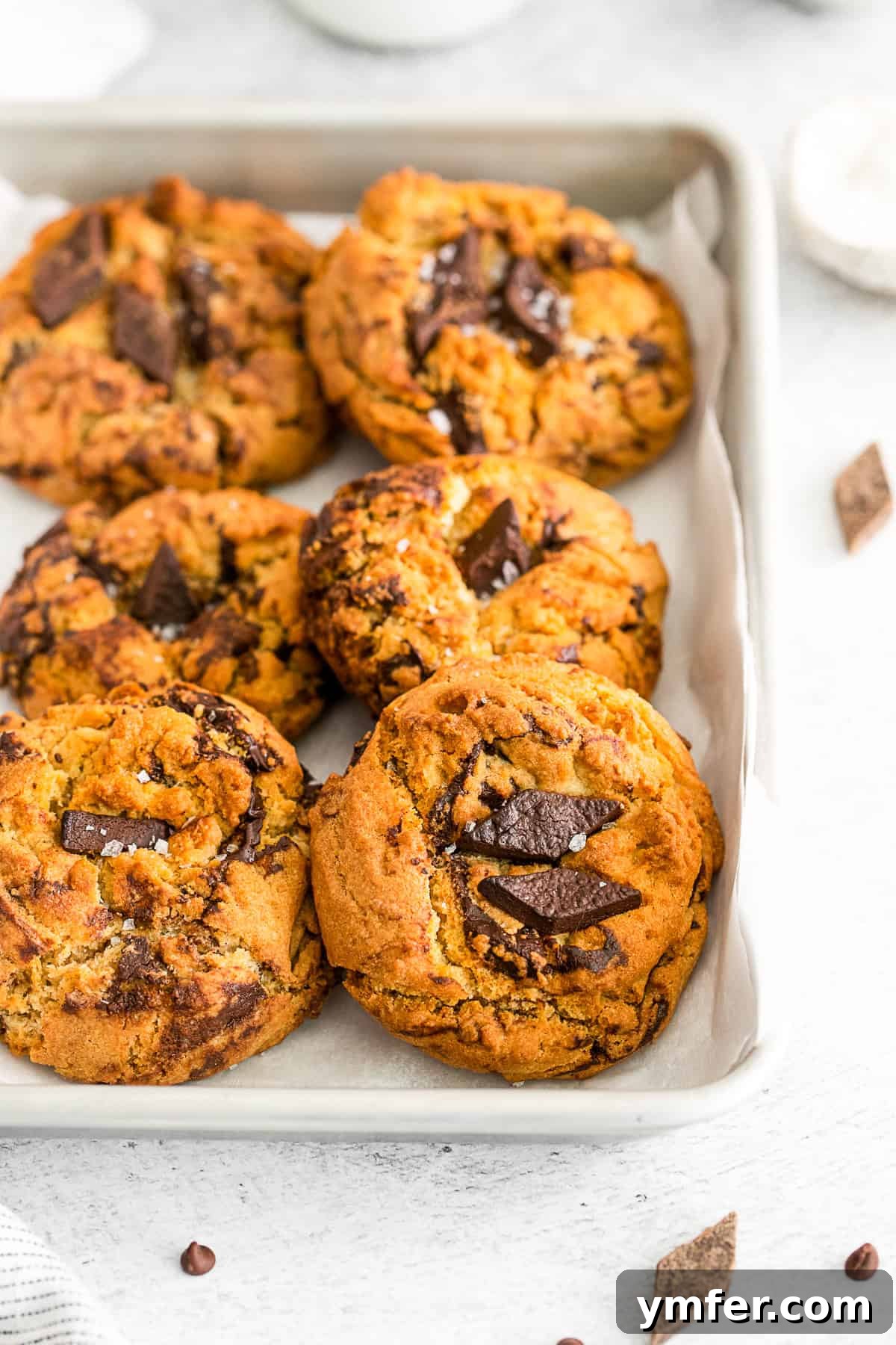 Six golden-brown air fryer chocolate chip cookies cooling on a parchment-lined sheet after baking, ready to be enjoyed.