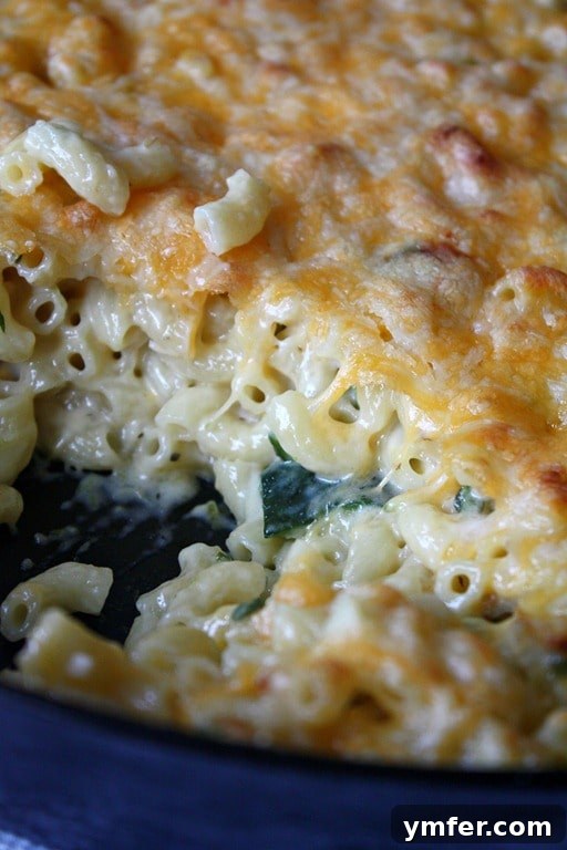 A serving of Poblano Macaroni and Cheese scooped from a skillet, showing off its creamy texture and bits of poblano pepper.