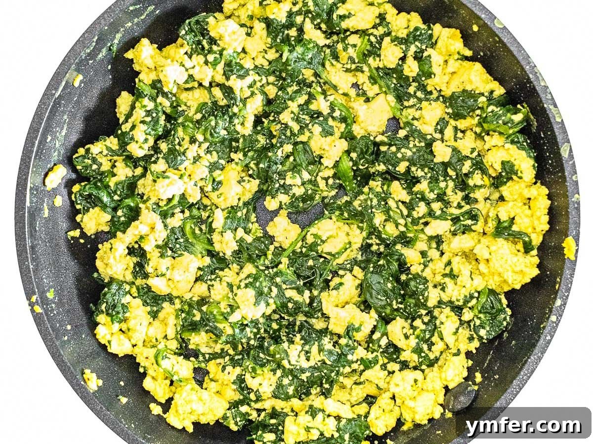 Plant-Powered Scramble 13 Fresh spinach cooking with crumbled tofu in a pan, showing a healthy and colorful combination.