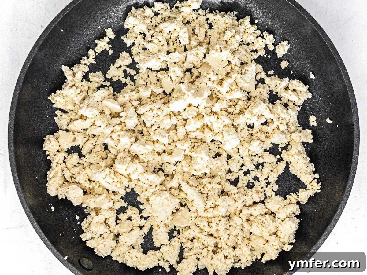 Plant-Powered Scramble 6 Crumbled tofu cooking in a pan with olive oil, showing the initial stage of the scramble preparation.