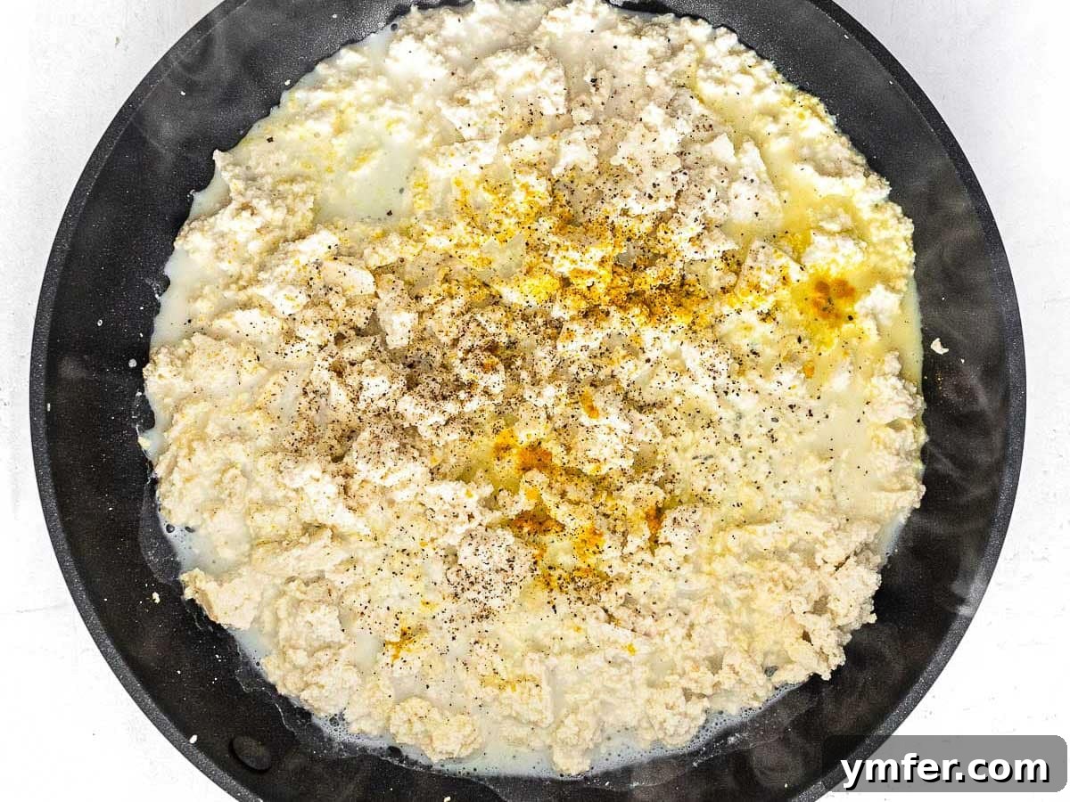 Plant-Powered Scramble 7 Turmeric, black salt, and plant milk being added to the cooking tofu scramble in the pan.