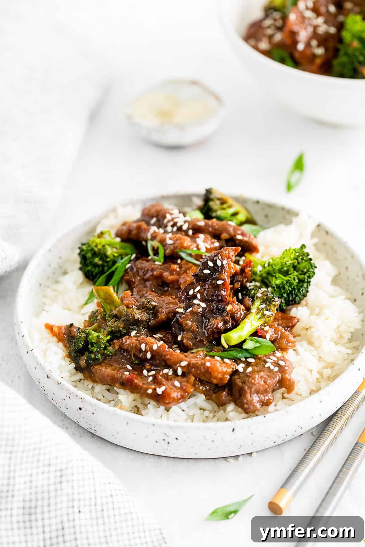 Speedy Instant Pot Mongolian Beef 5 A close-up of Mongolian beef in a bowl with rice and broccoli, garnished with green onions and sesame seeds.
