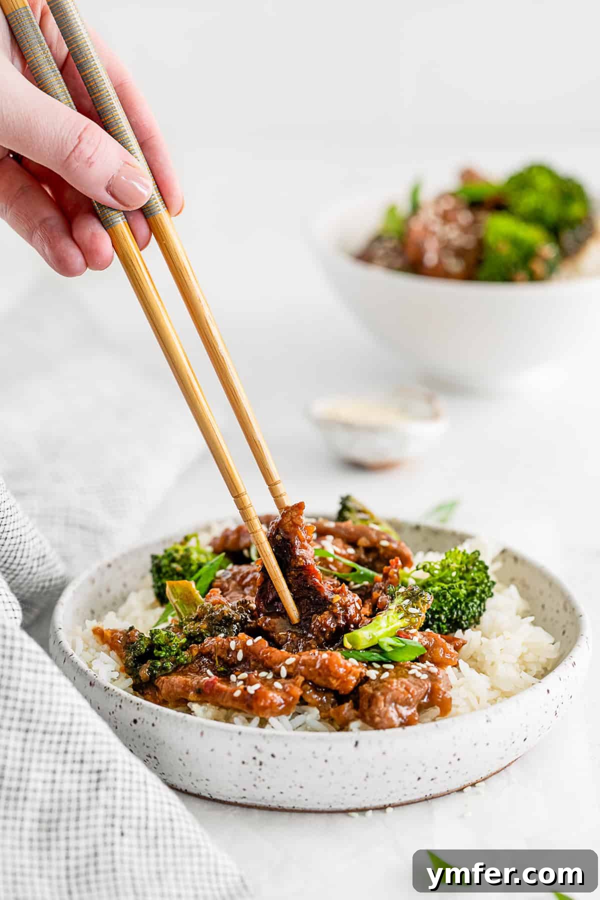 Speedy Instant Pot Mongolian Beef 6 Mongolian beef in a bowl with chopsticks grabbing a piece of meat, showing its tender texture.