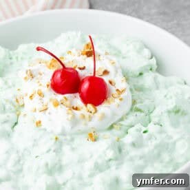 Watergate Salad in a white bowl topped with cherries. A vibrant green, fluffy dessert ready to be enjoyed.