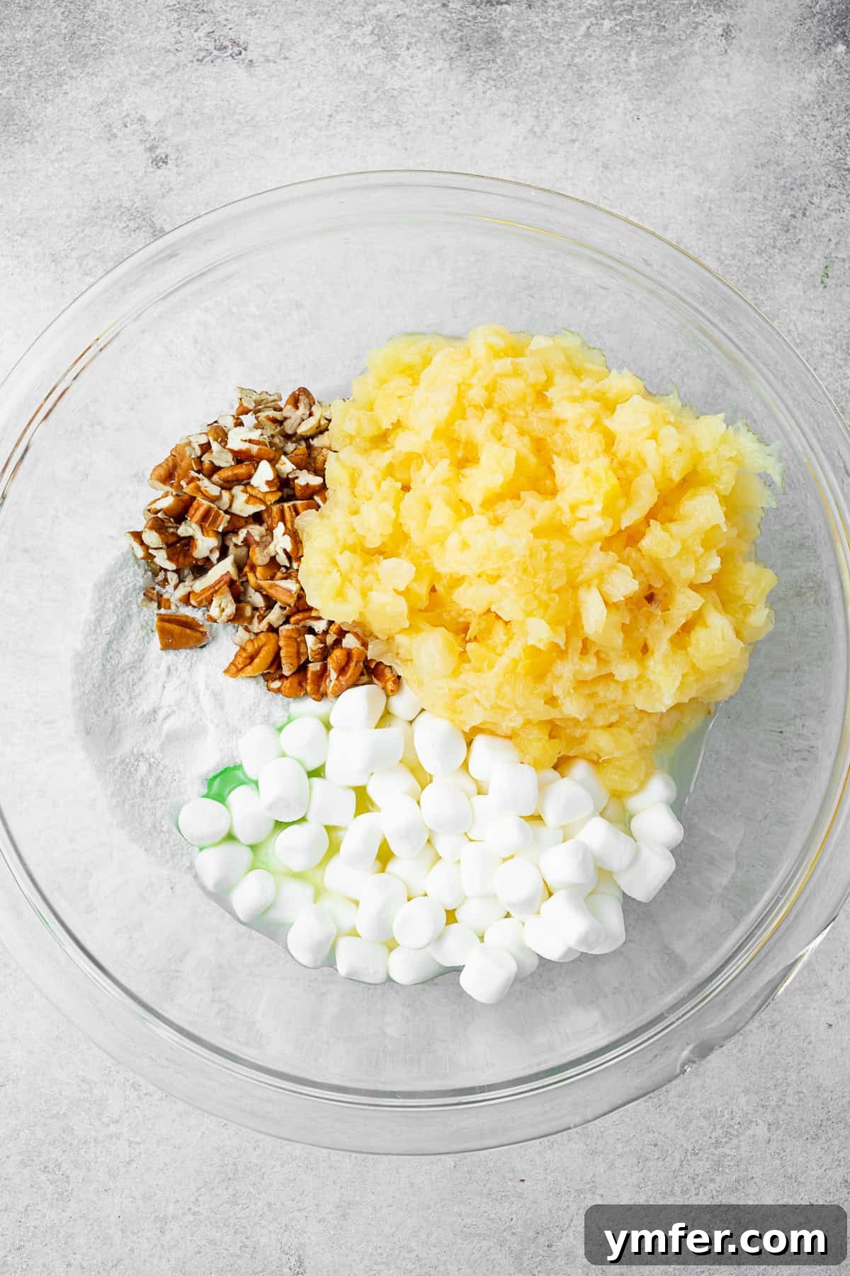 Emerald Pineapple Dream 4 A bowl filled with crushed pineapple, miniature marshmallows, pecans, and pistachio pudding mix, ready to be mixed.