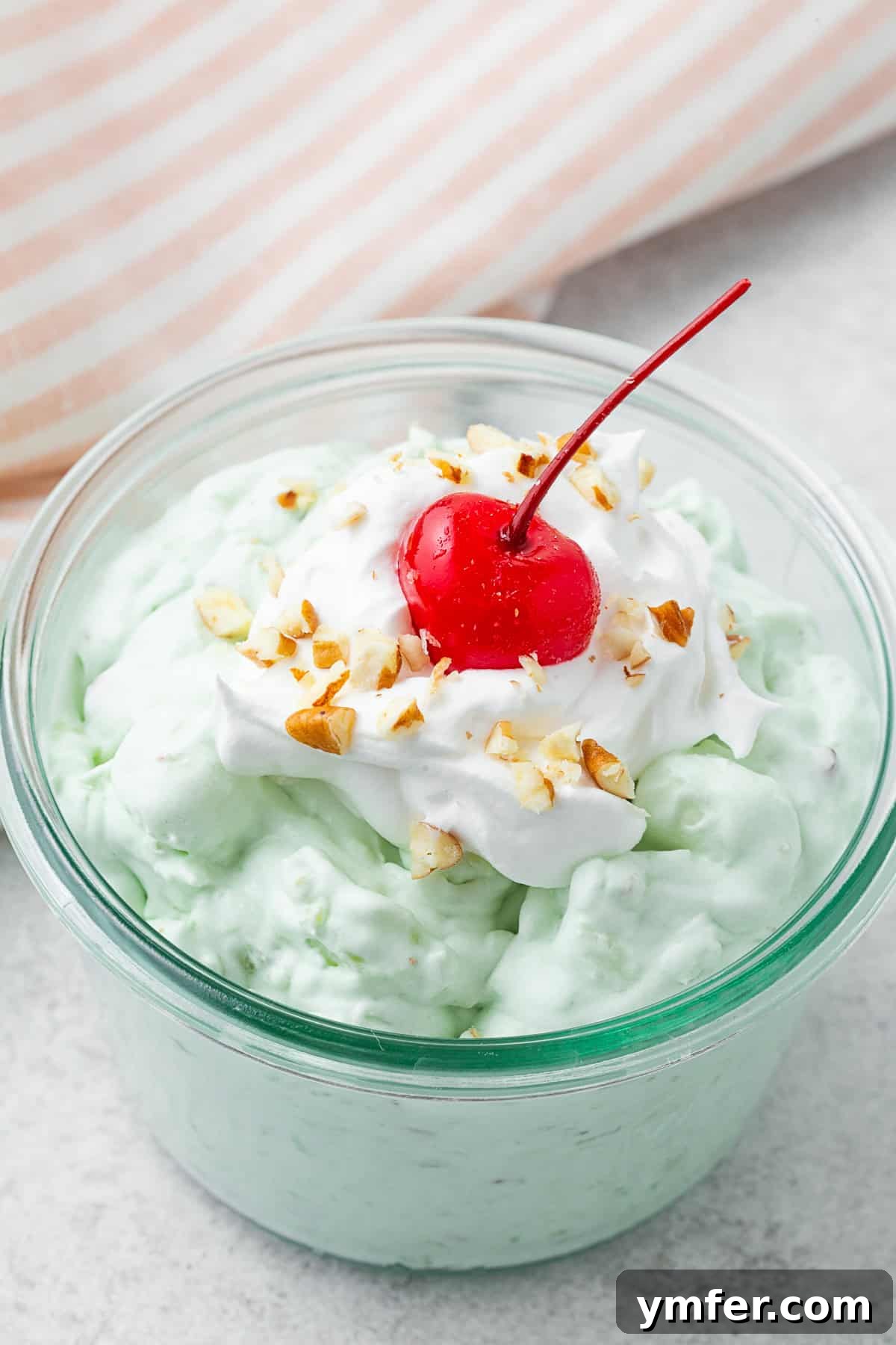 Emerald Pineapple Dream 6 Watergate Salad in a bowl topped with whipped cream, pecans, and a cherry. A close-up view of the fluffy texture.