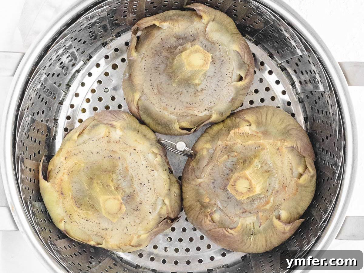 Artichokes steaming gently in a basket within a covered pot, indicating the cooking process.