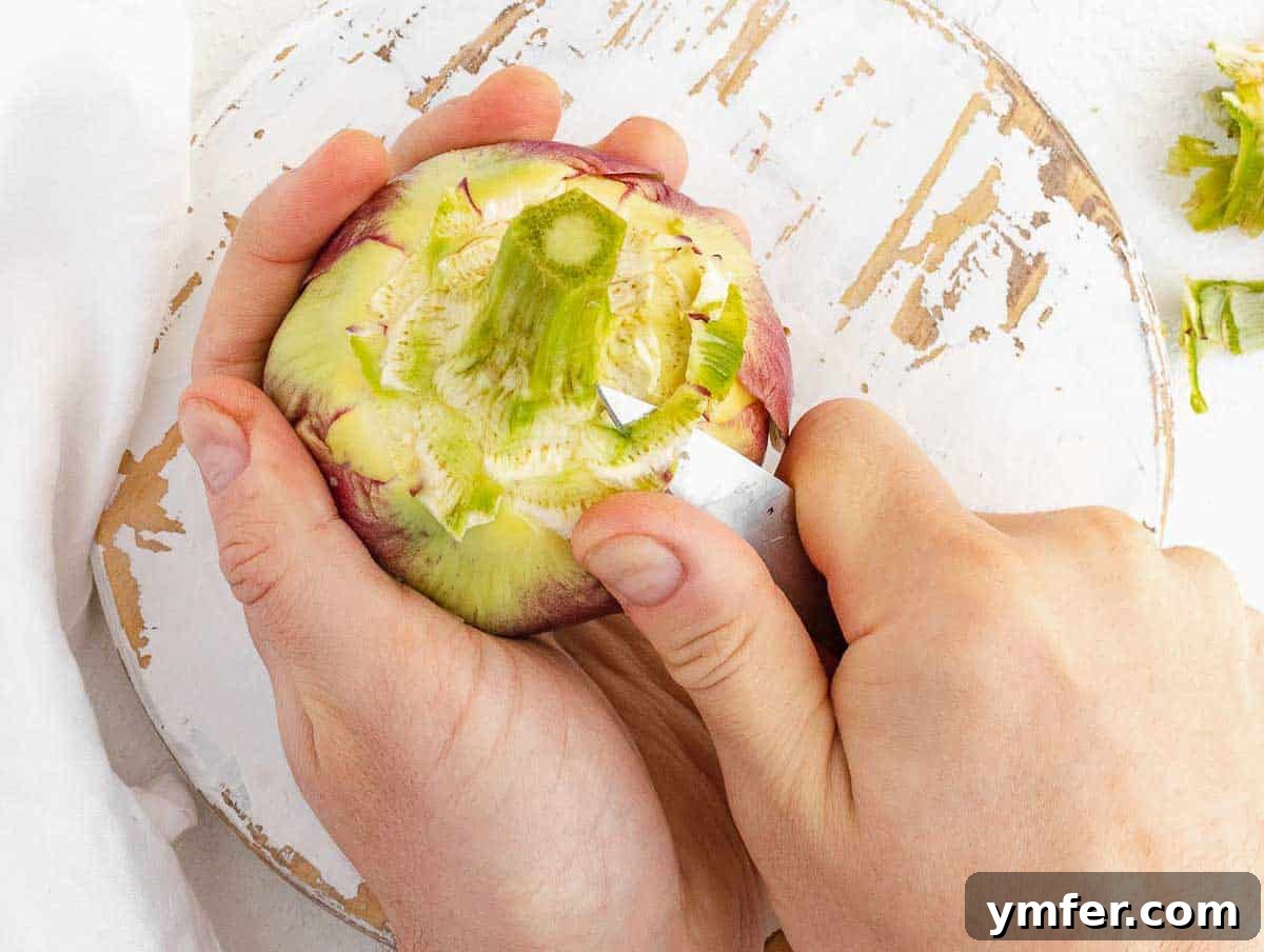 A close-up of hands cleaning the stem of an artichoke with a paring knife.