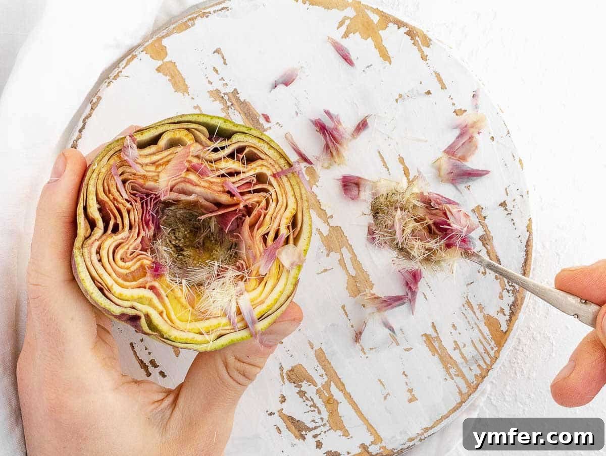 Hands carefully removing the fuzzy choke from the center of an artichoke with a small spoon.