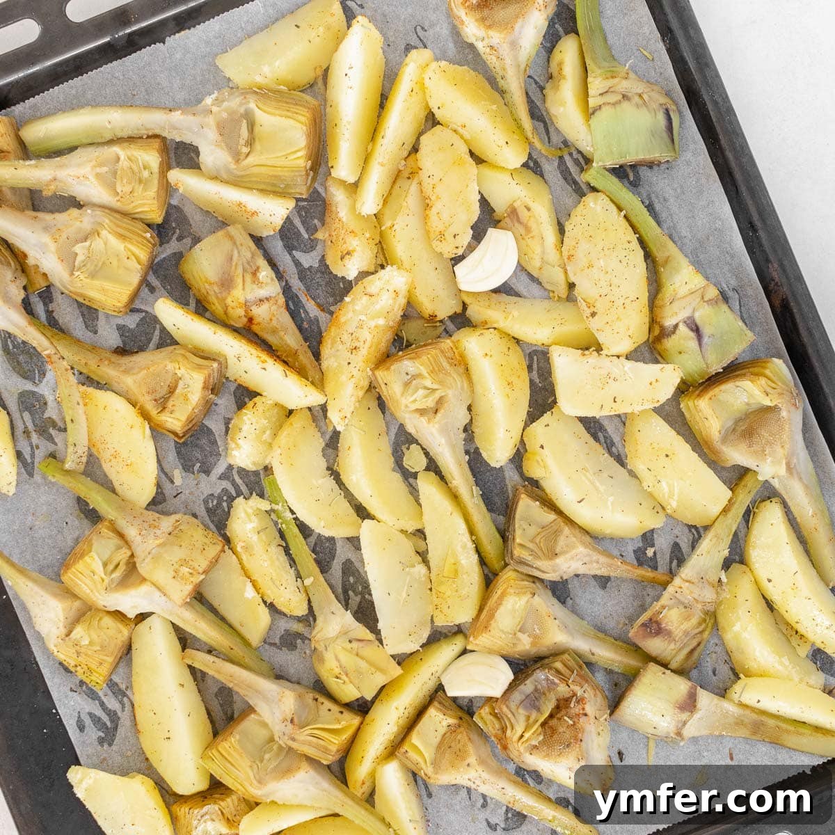 Artichokes and potatoes tossed with olive oil and spices on a baking tray