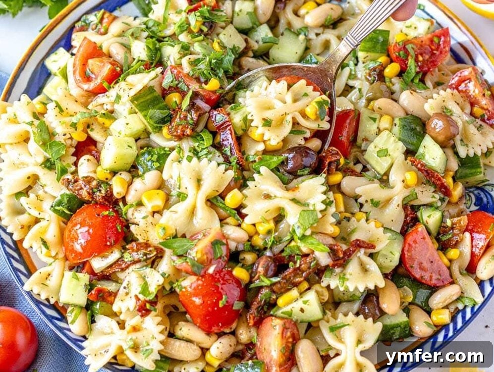Vibrant Vegan Pasta Salad 8 Delicious Vegan Pasta Salad on a blue plate with a hand holding a silver spoon, ready to enjoy.