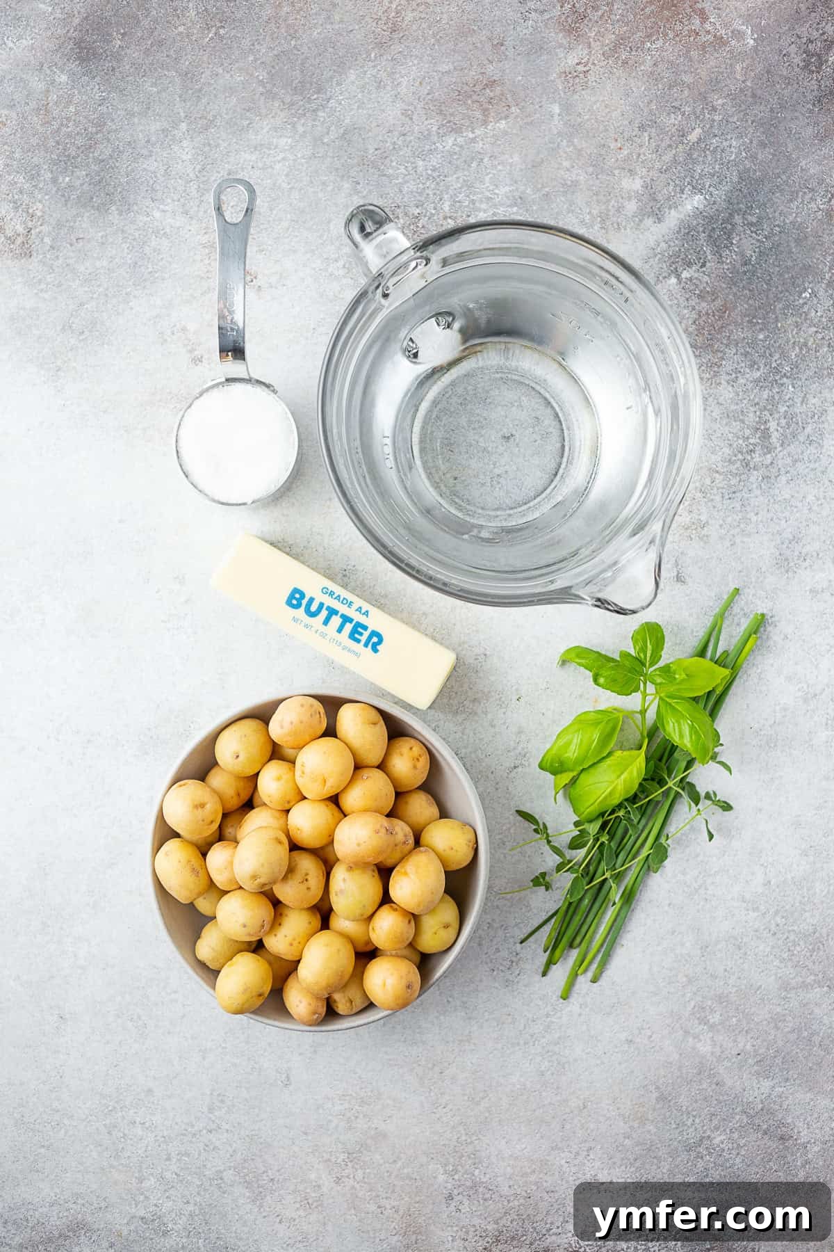 Ingredients for Syracuse Salt Potatoes: baby potatoes, water, fresh herbs, butter, and kosher salt laid out on a table.