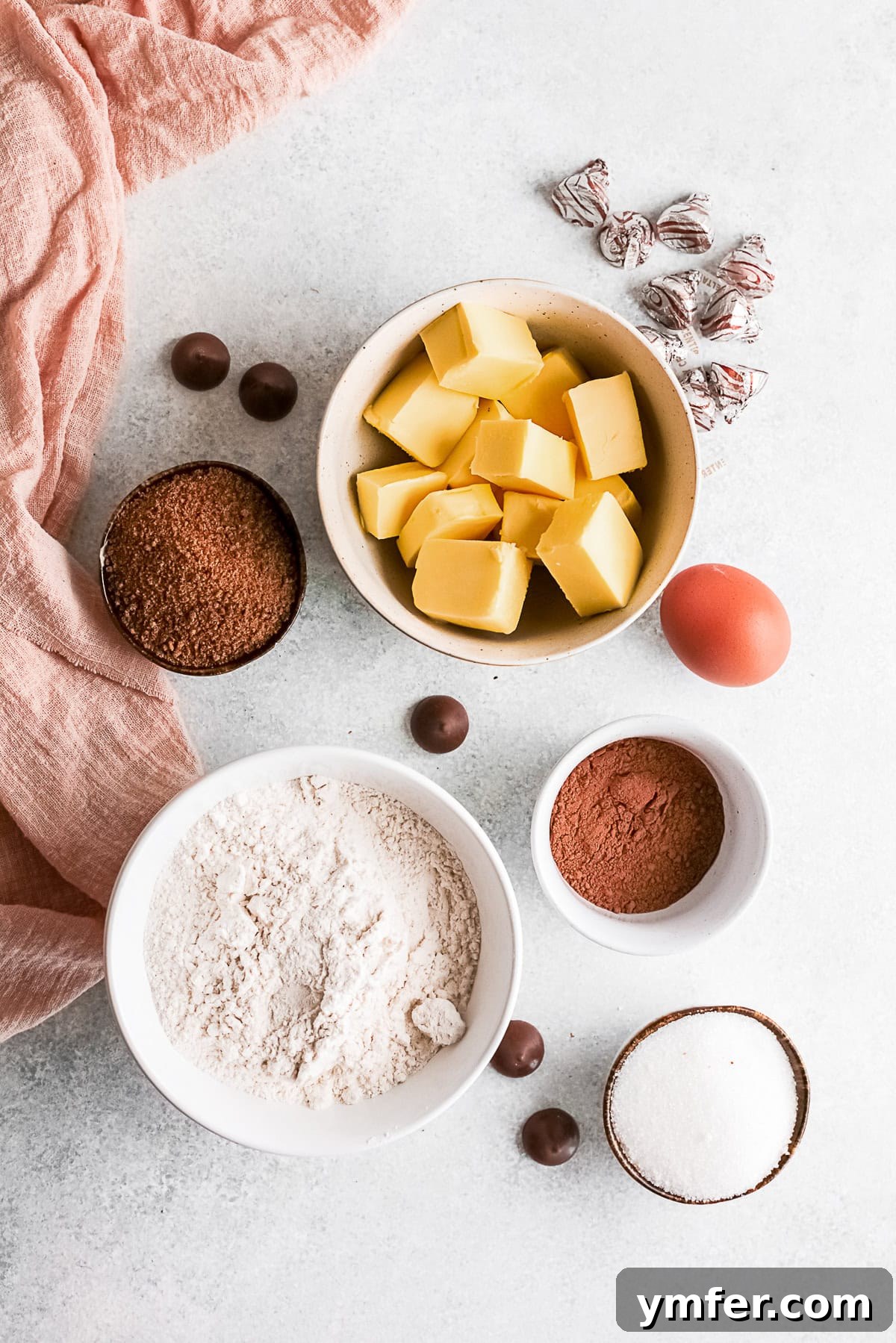Chocolate Kissed Delights 3 An array of ingredients including brown sugar, egg, butter, flour, granulated sugar, unsweetened cocoa powder, and Hershey's Kisses beautifully arranged on a rustic wooden table, ready for baking.