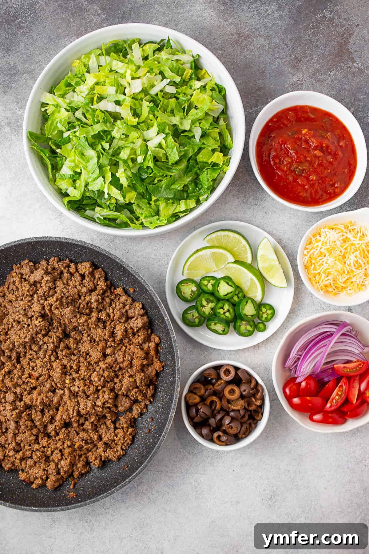 Speedy Taco Salad Delight 3 A vibrant display of taco salad ingredients: ground taco meat, crisp lettuce, salsa, cheese, onions, tomatoes, olives, peppers, and fresh limes, ready for assembly.