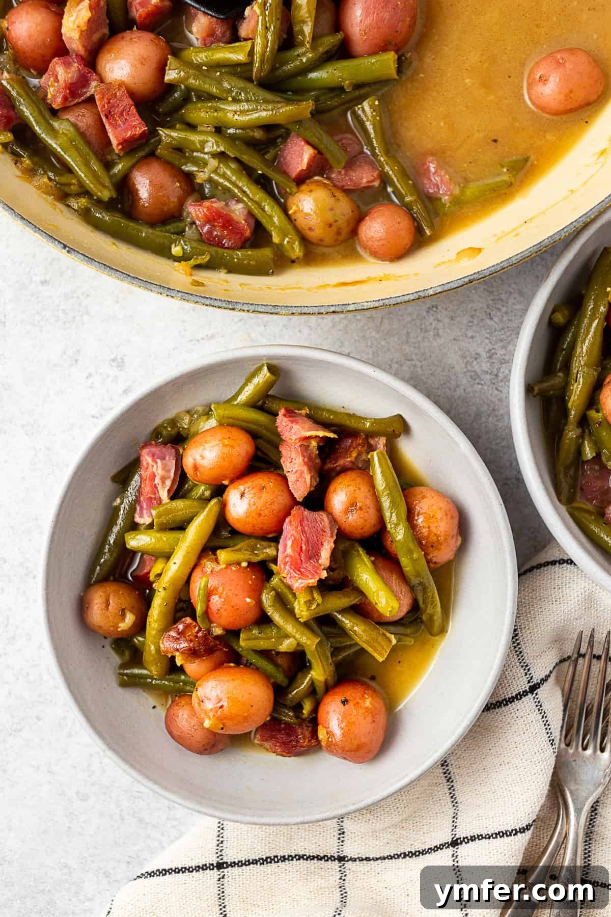 Down-Home Southern Green Beans and Potatoes 2 Grey bowl filled with green beans, ham, and potatoes on a table with a napkin.