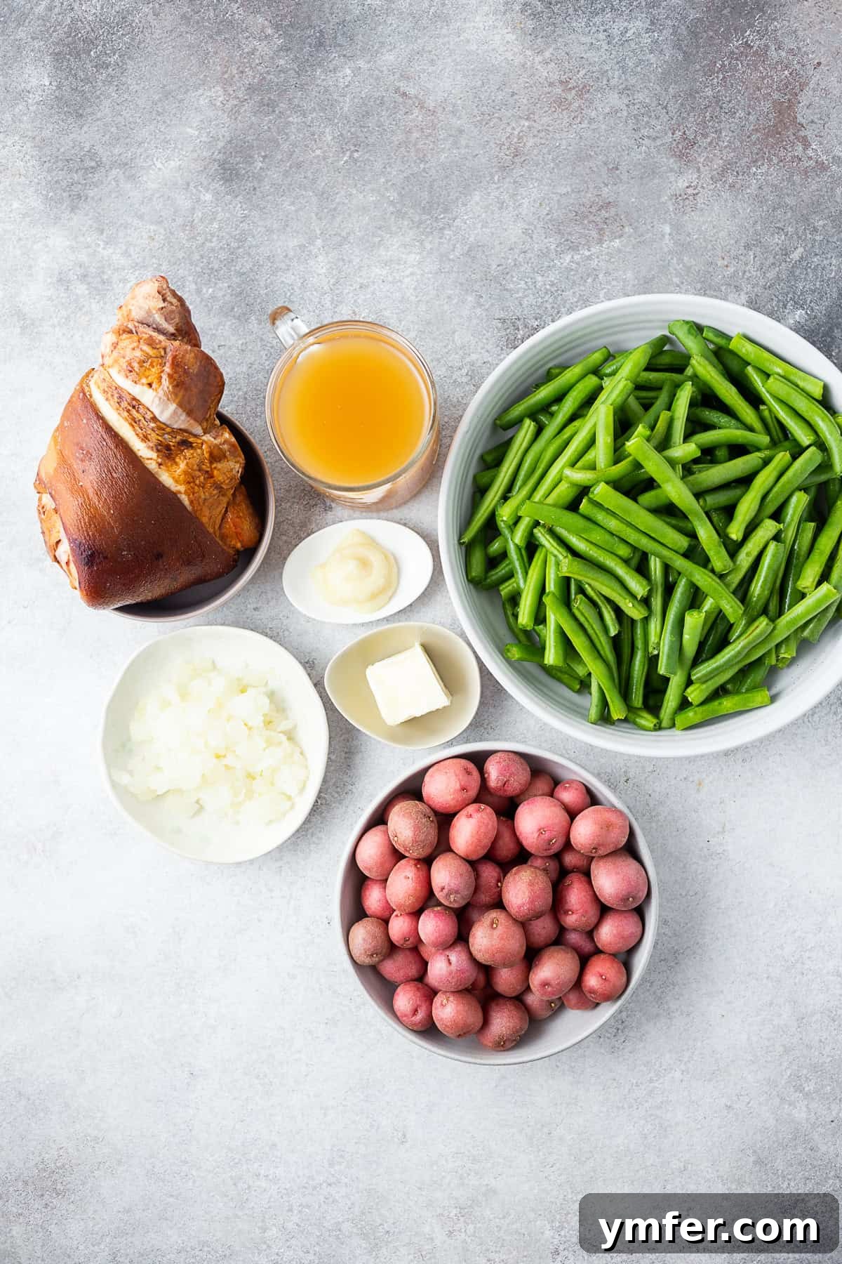 Down-Home Southern Green Beans and Potatoes 3 Ham hock, beans, potatoes, chicken stock, garlic, butter, and onion on a table.